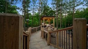 Une terrasse en bois mène à un belvédère entouré de grands arbres.