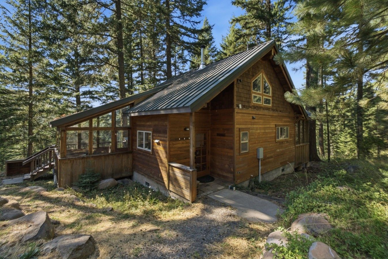 A wooden cabin with a large windowed porch, surrounded by a forest.
