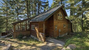 A wooden cabin with a large windowed porch, surrounded by a forest.