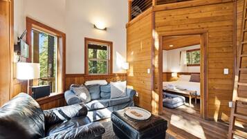 A cozy cabin interior with a sofa, ottoman, and a bed in the adjacent room.