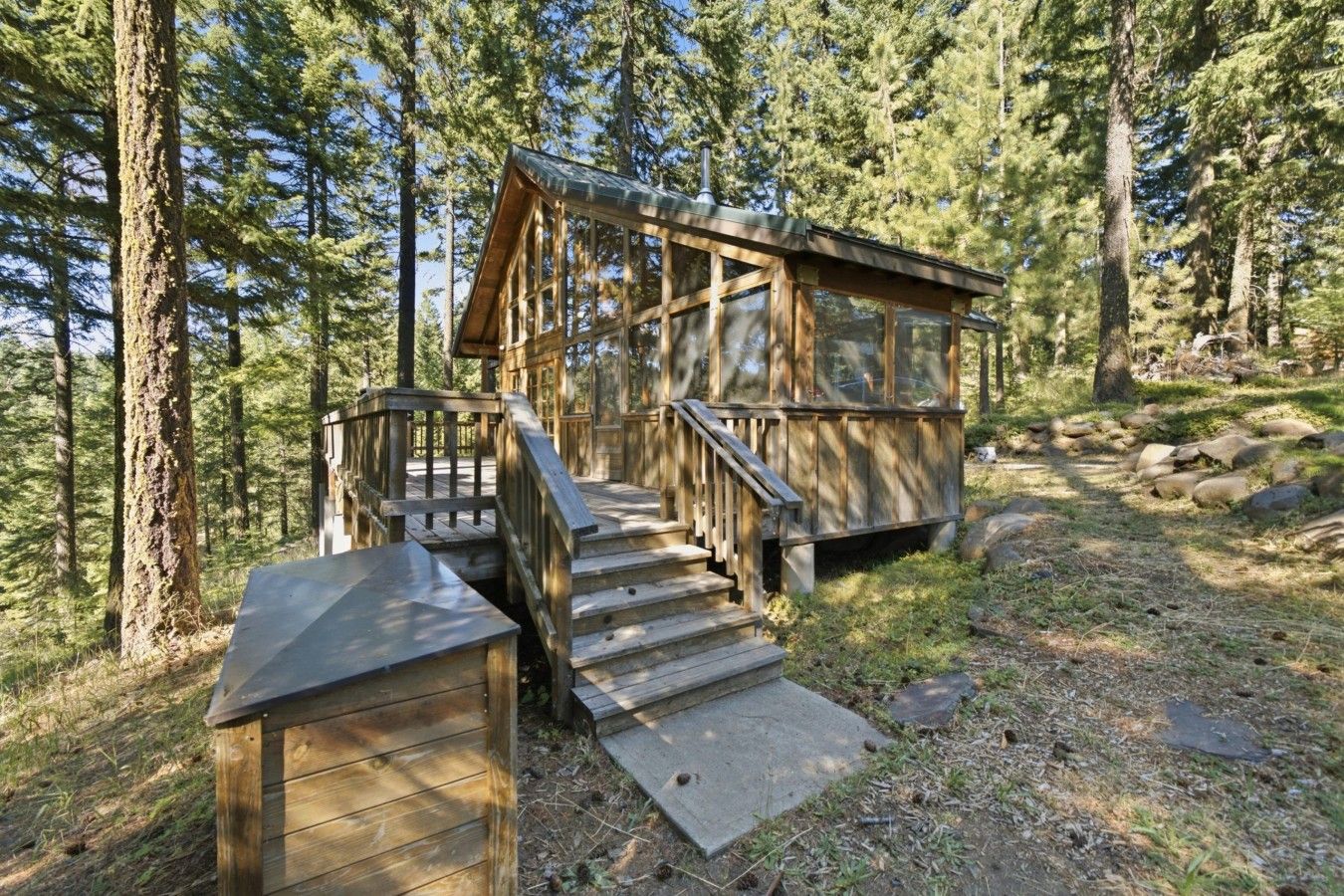 A wooden cabin with a staircase leading to a deck, surrounded by a forest.