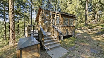 A wooden cabin with a staircase leading to a deck, surrounded by a forest.