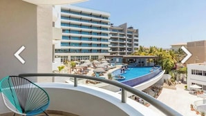 Un hotel moderno con área de piscina, un balcón con una silla y vistas de los edificios circundantes.