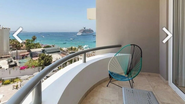 Un balcón con vistas al mar y un crucero, una silla y una ventana con cortina.