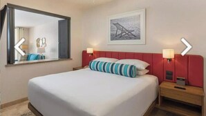 Habitación de hotel con una cama grande, un ventilador de techo, un cuadro enmarcado en la pared y dos lámparas de noche.