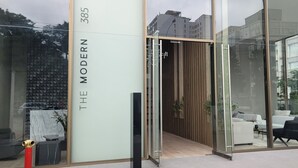 Ein moderner Gebäudeeingang mit Glasfassade, Holzinnenarchitektur und einem sichtbaren Außenbereich mit Sitzgelegenheiten.