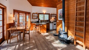 A cozy cabin interior with a wooden dining area, kitchen, and a wood-burning stove. - Soda Mountain Cabin w/ Jacuzzi and Wood Stove at Green Springs Inn (Ashland)