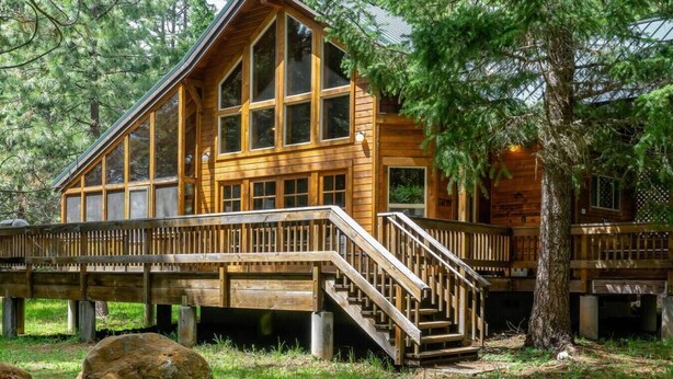 A wooden cabin with a deck and stairs, surrounded by trees. - Soda Mountain Cabin w/ Jacuzzi and Wood Stove at Green Springs Inn (Ashland)