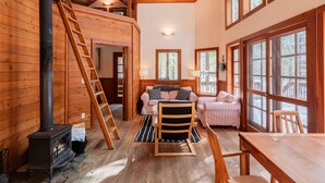 A cozy cabin interior with a loft bedroom, a central seating area with a sofa and chairs, a dining table, and a wood-burning stove. - Soda Mountain Cabin w/ Jacuzzi and Wood Stove at Green Springs Inn (Ashland)