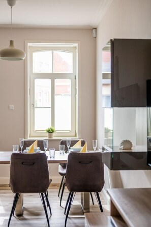 A dining area with a table set for four, two chairs, a hanging light fixture, and a window with a view of buildings.