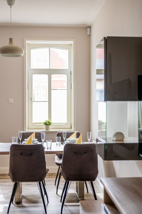 A dining area with a table set for four, two chairs, a hanging light fixture, and a window with a view of buildings.