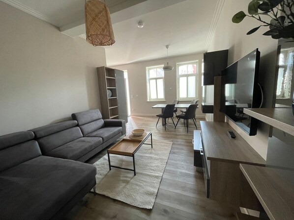 Una sala de estar moderna con un sofá gris, una mesa de centro, un televisor y un comedor con sillas y una mesa.
