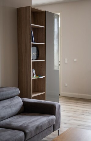 Una sala de estar moderna con un sofá gris, una estantería de madera y una ventana con persianas.