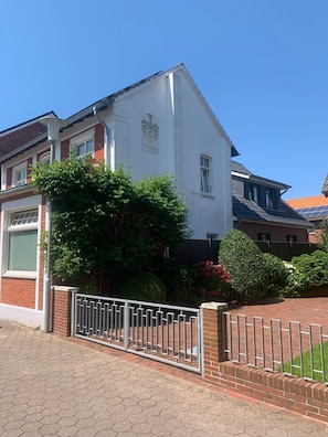 A two-story house with a white facade, a brick lower level, and a metal gate in front.