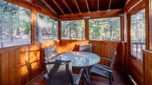Eine Holzhütte mit einem runden Glastisch und vier Stühlen, großen Fenstern und Blick auf einen Wald.