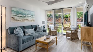 A modern living room with a grey sofa, wicker chairs, a wooden coffee table, and a ceiling fan.