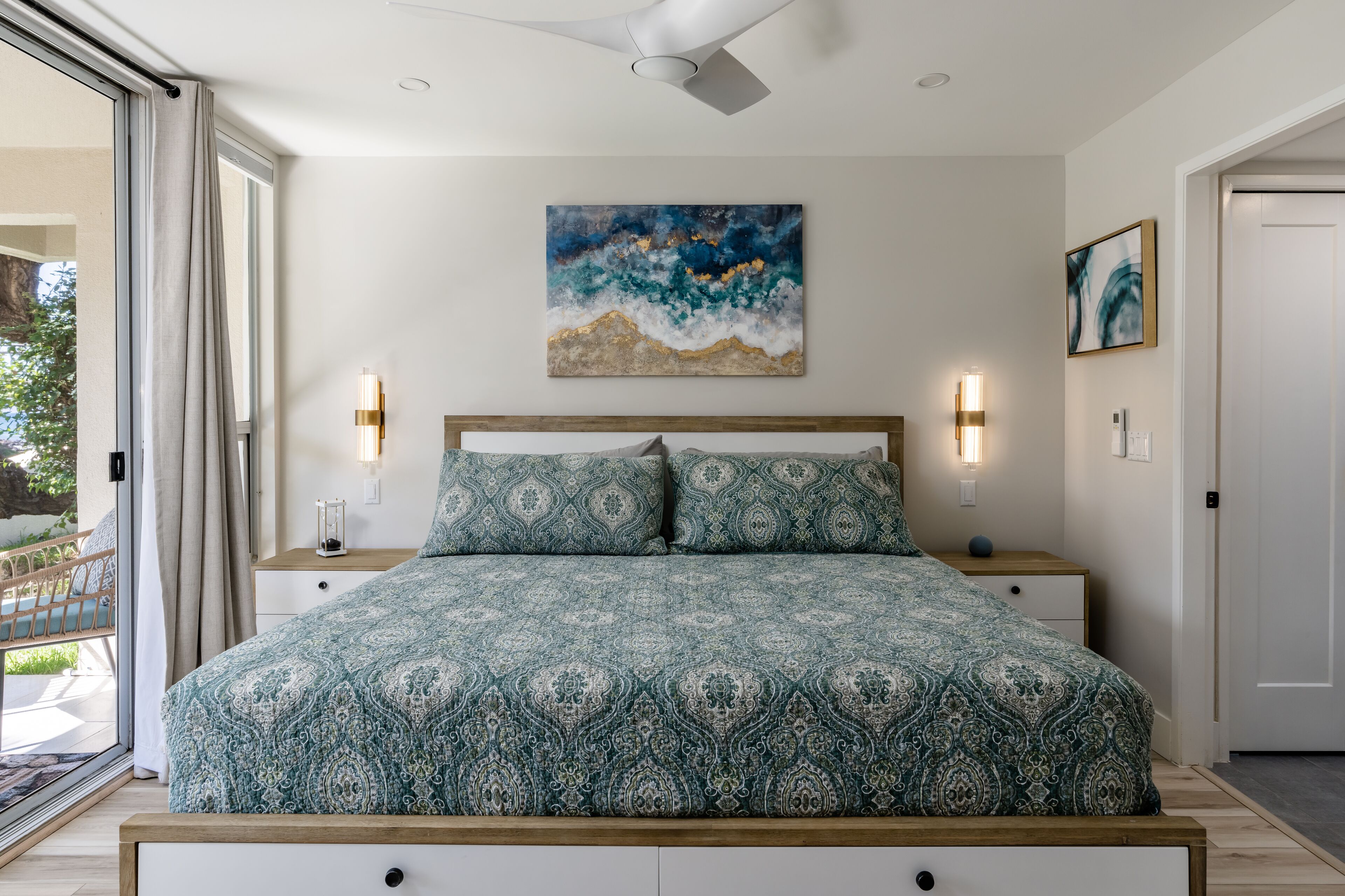 A bedroom with a patterned bedspread, a ceiling fan, and artwork on the walls.