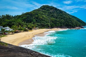 A beach with a sandy shore, clear turquoise waters, and a lush green hill in the background.