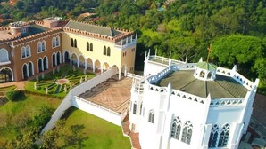 An aerial view of a castle with a large courtyard, a beach in the background, and a white building with a cross on top. - Severos mar 2 (Ubatuba)