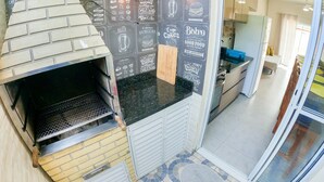 A kitchen with a built-in brick oven, a chalkboard menu, and a sliding glass door leading to a dining area. - Severos mar 2 (Ubatuba)