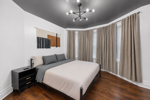 A bedroom with a bed, bedside tables, a modern chandelier, and large windows with curtains.