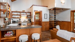 A compact kitchen with wooden cabinetry, a central island with stools, a built-in stove, and a staircase with a wooden railing. - Boccard Point Cabin w/ Jacuzzi and Wood Stove at Green Springs Inn (Ashland)