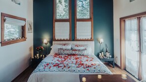 A bedroom with a large bed, two windows, a wooden ceiling, and a nightstand with candles. - Boccard Point Cabin w/ Jacuzzi and Wood Stove at Green Springs Inn (Ashland)