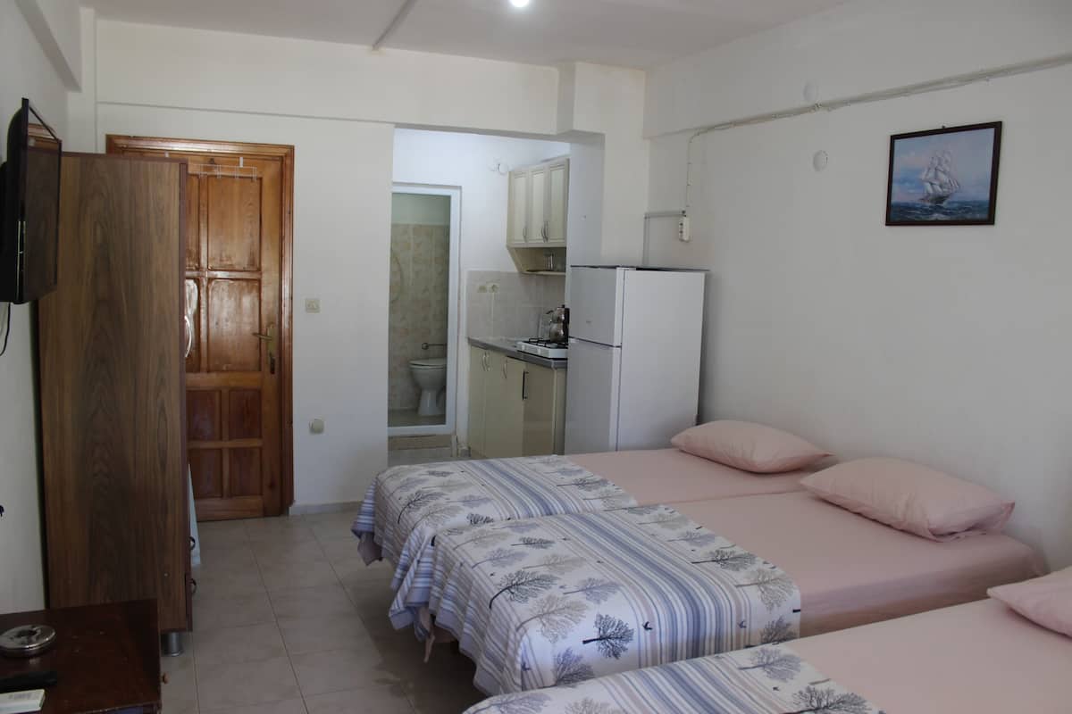 A bedroom with two beds, a wooden wardrobe, a white refrigerator, and a bathroom visible through an open door.