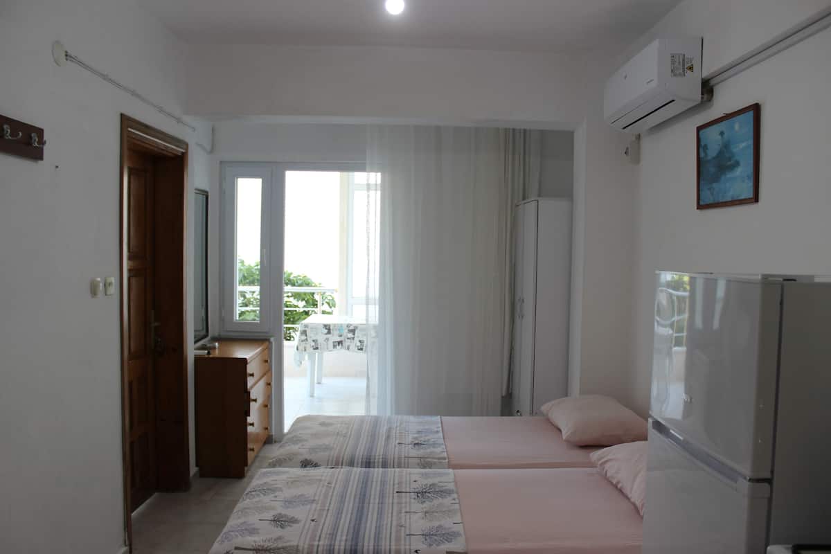 A bedroom with two beds, a dresser, a refrigerator, and a window with curtains.