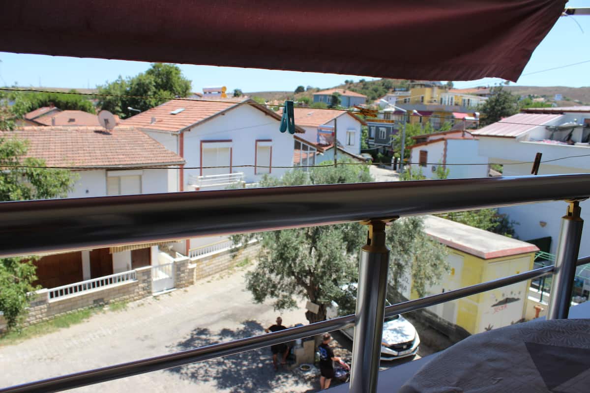A residential street view with houses, a tree, and a metal railing.