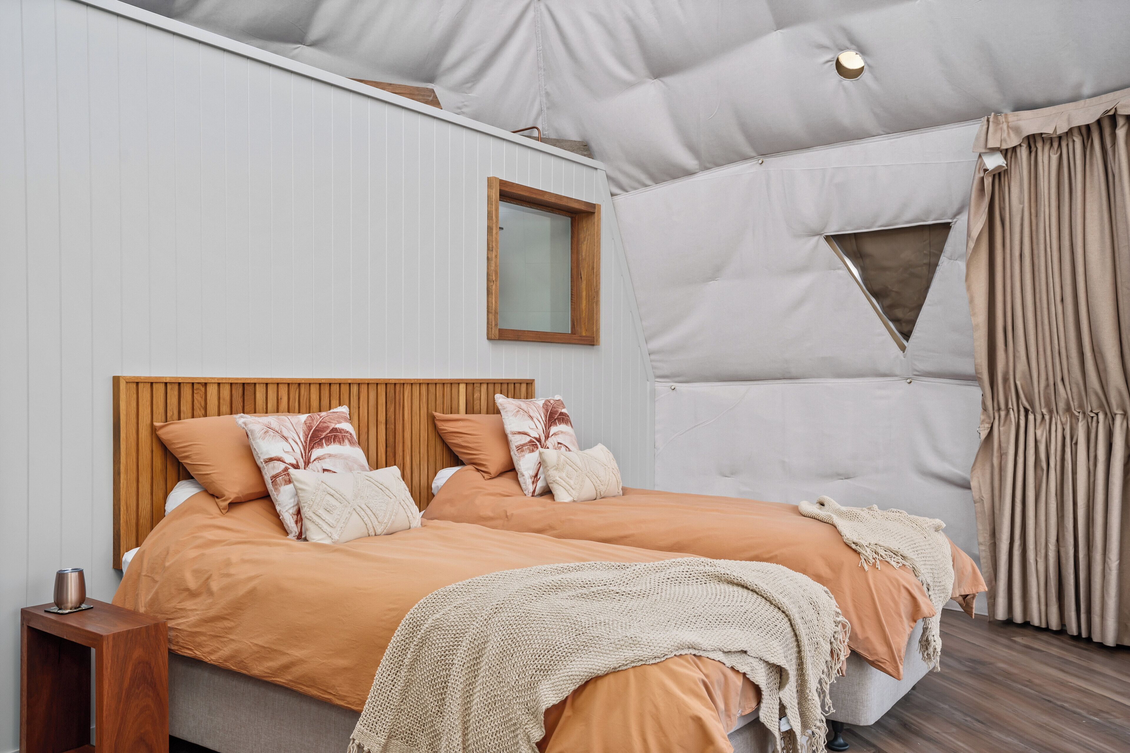 A bedroom with a wooden headboard, two beds, a window, and a curtain.
