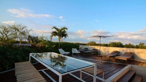 Una terrazza sul tetto con tavolo in vetro, poltrone relax e un pavimento in legno.