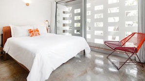 Una camera da letto moderna con un letto grande, una poltrona rossa e una porta vetrata scorrevole che dà su un balcone.