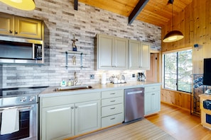 Enjoy cooking in this well-equipped kitchen with a range hood, microwave, and dishwasher, set against a brick-patterned backsplash and wooden ceiling.