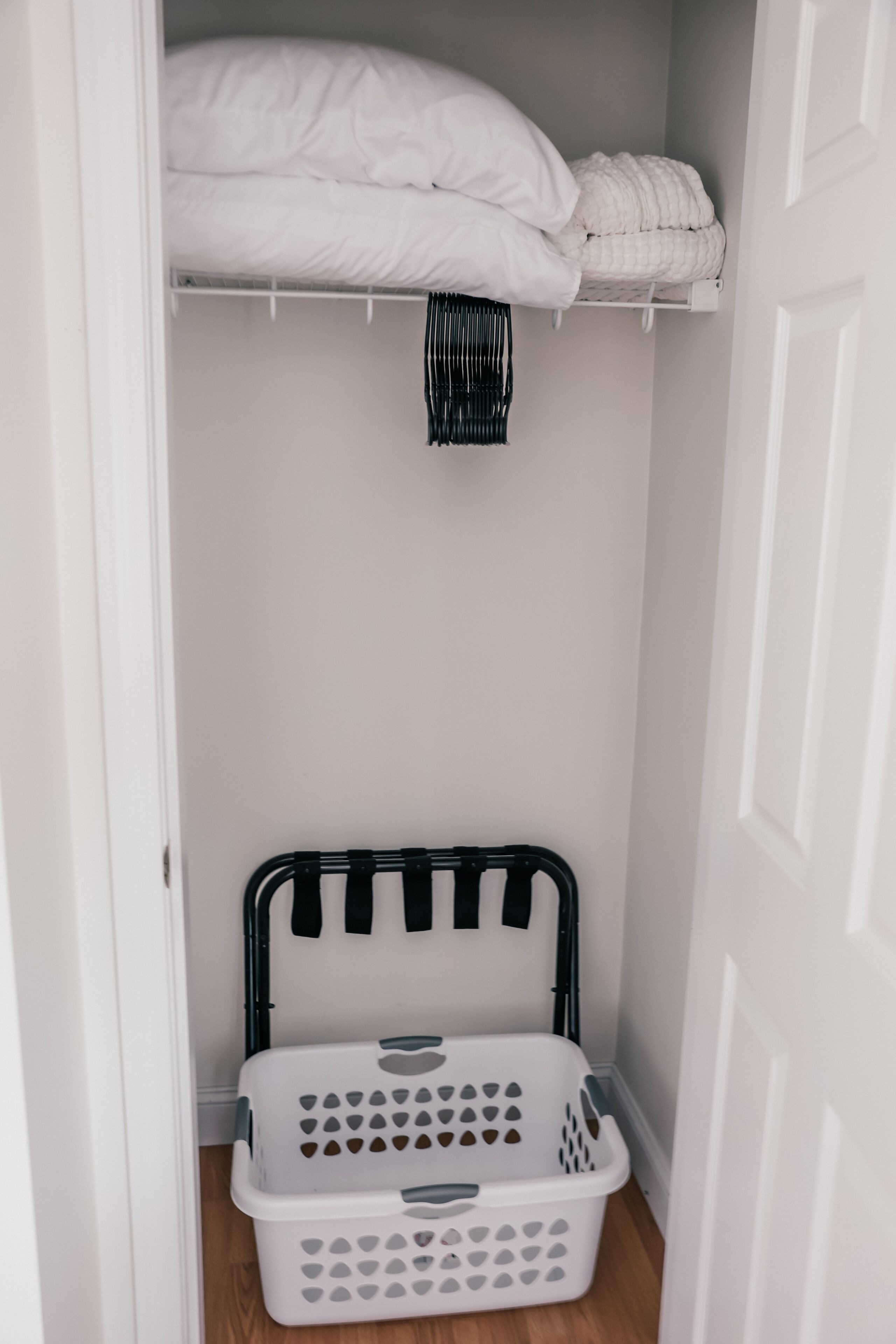 Une buanderie avec un lit blanc, un étendoir et deux paniers à linge blancs.