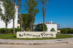 Un panneau indiquant l’entrée du parc de Marina, avec un bâtiment moderne en arrière-plan.