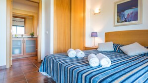 A hotel room with a bed, a nightstand, a lamp, a painting, and a bathroom with a sink and cabinets. - Great and Spacious apartment overlooking the Swimming-Pool (Lagos)