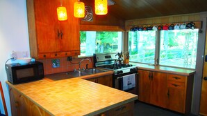 A kitchen with wooden cabinets, a microwave, a stove, and a sink. There are hanging lights and a window with a view of greenery outside.