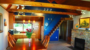 A spacious dining area with a wooden table and chairs, a kitchen in the background, and a stone fireplace.