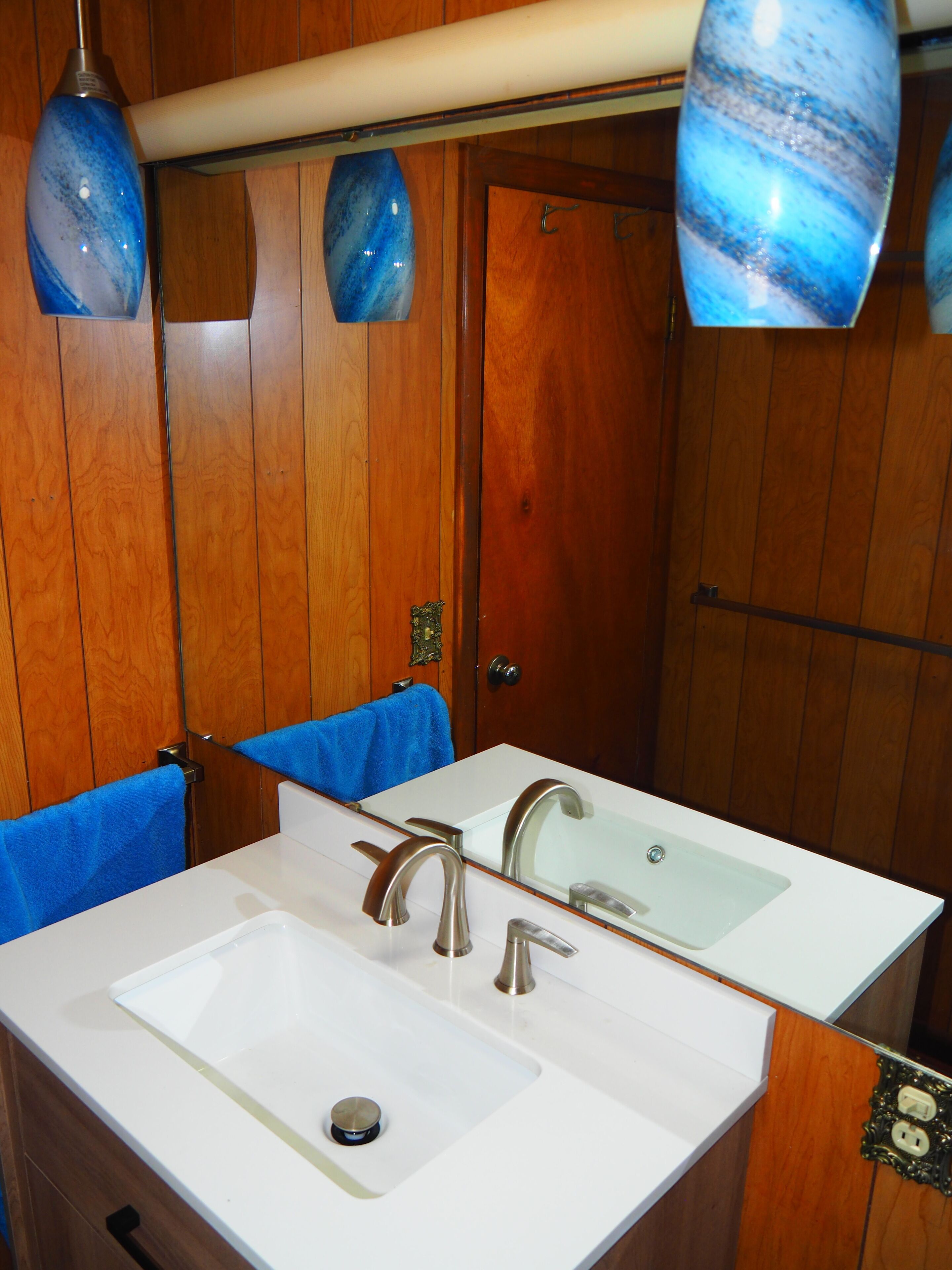 A bathroom with wooden paneling, a white sink with two faucets, and a mirror above the sink.