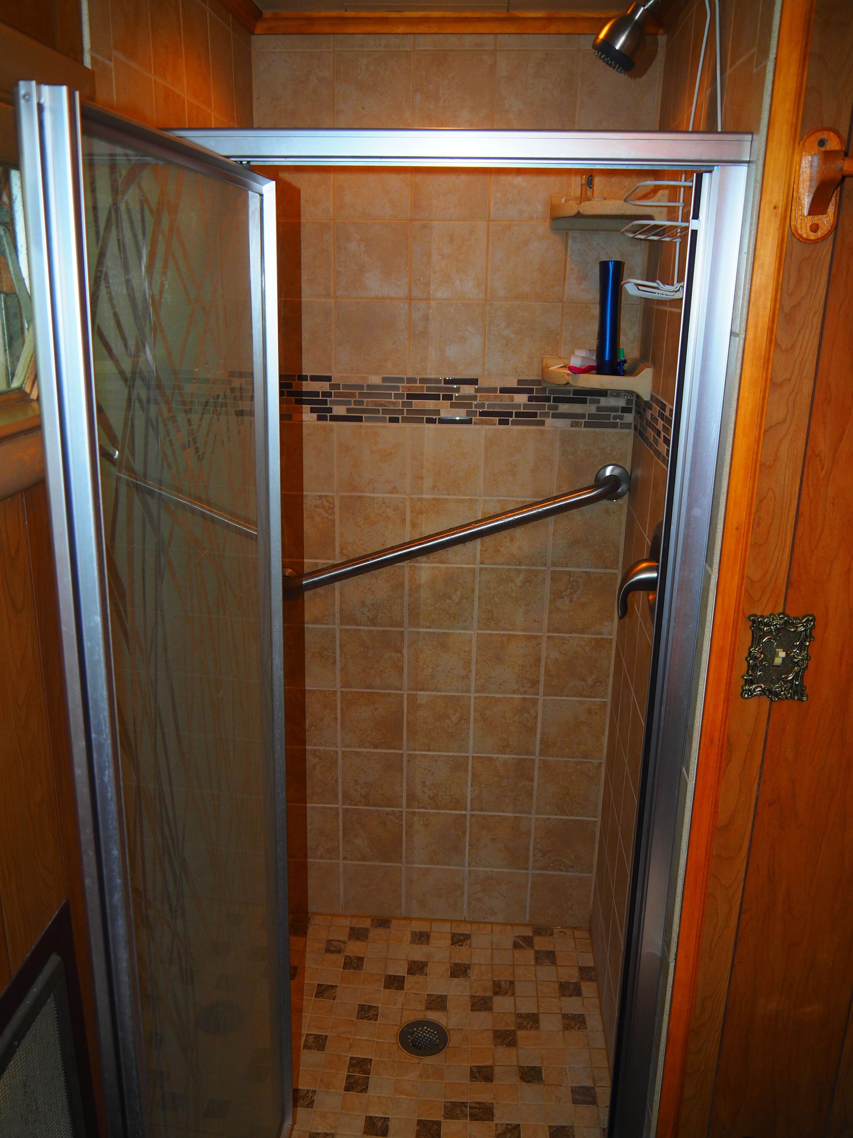 A shower stall with a glass door, a handrail, and a tiled floor.
