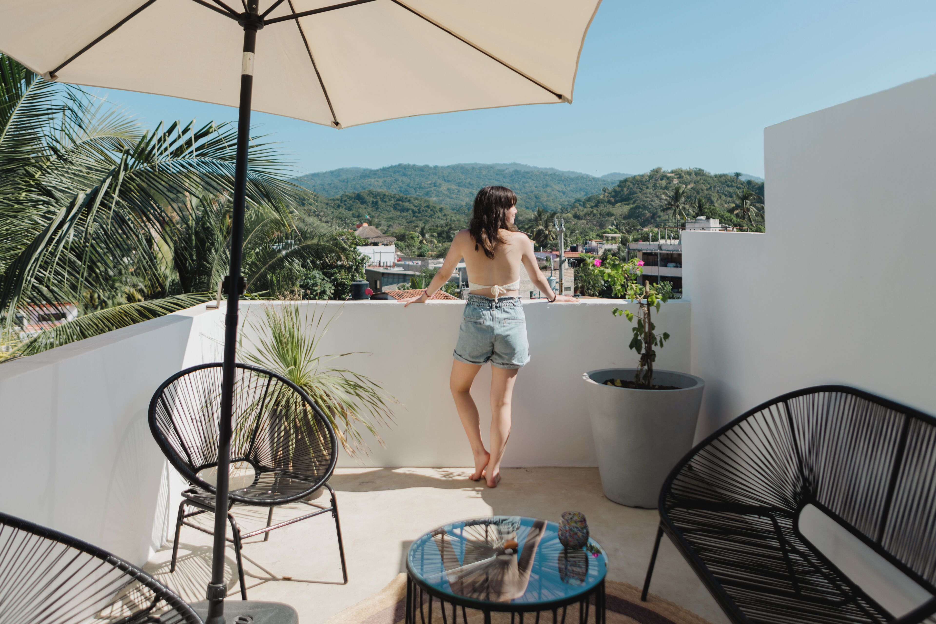 Un balcon avec vue sur les montagnes, une plante en pot et deux chaises noires.