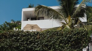 A modern building with a white facade, a balcony with a beige umbrella, and a palm tree. - Casa Fénix - Sayulita (Sayulita)