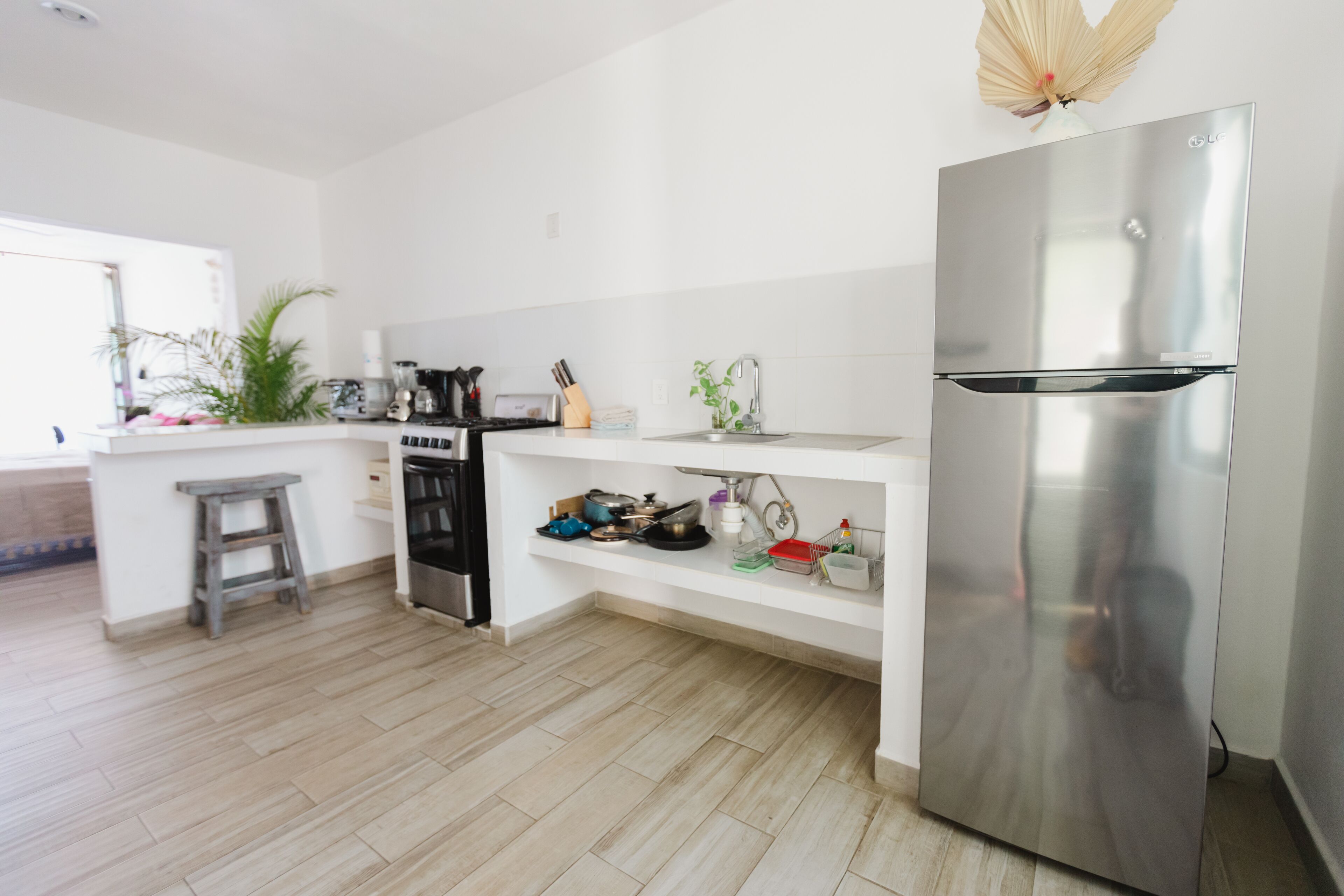 Una cucina moderna con frigorifero in acciaio inossidabile, forno integrato e lavello. Si nota uno sgabello di legno e uno scaffale con utensili da cucina.