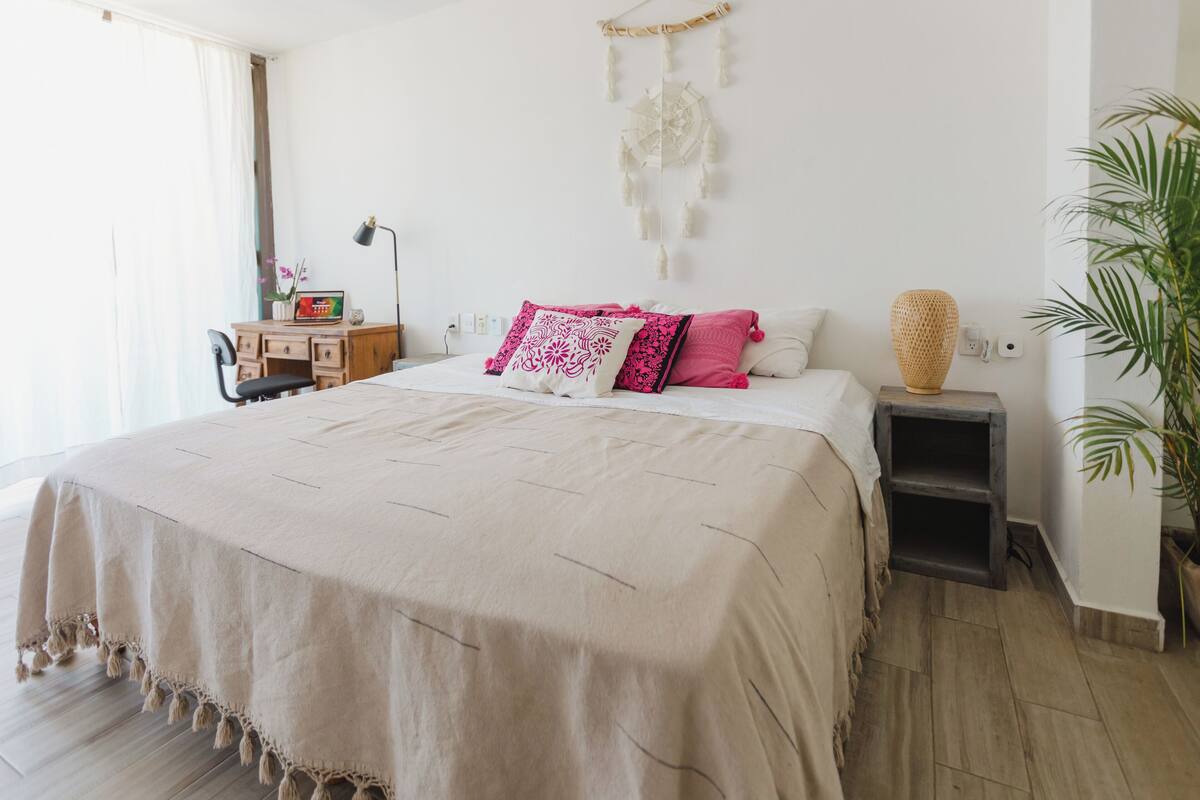 Un dormitorio con cama, mesitas de noche, un escritorio, una silla y un atrapasueños colgante.