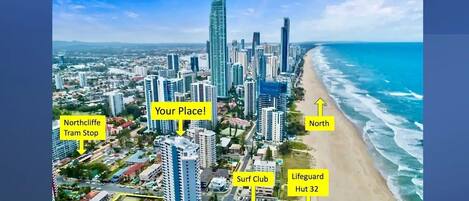 An aerial view of a coastal city with high-rise buildings, a beach, and labeled landmarks such as Northcliffe Tram Stop, Surf Club, and Lifeguard Hut 32.