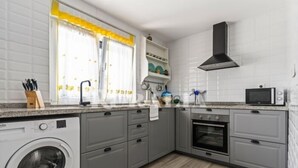 Een kleine keuken met een wasmachine, oven, magnetron en grijze kastjes.