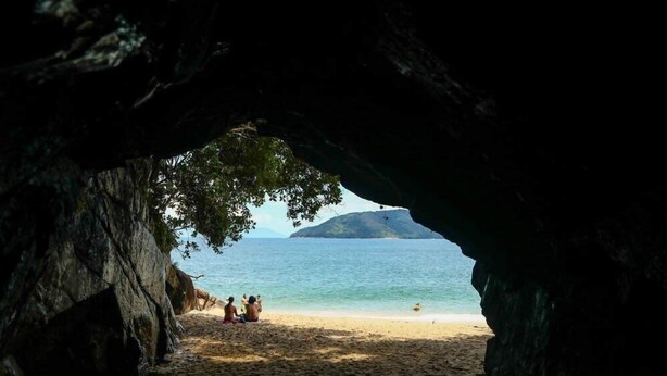 A beach scene viewed through a cave entrance with a clear view of the sea and a distant island. - Geneis  (Ubatuba)