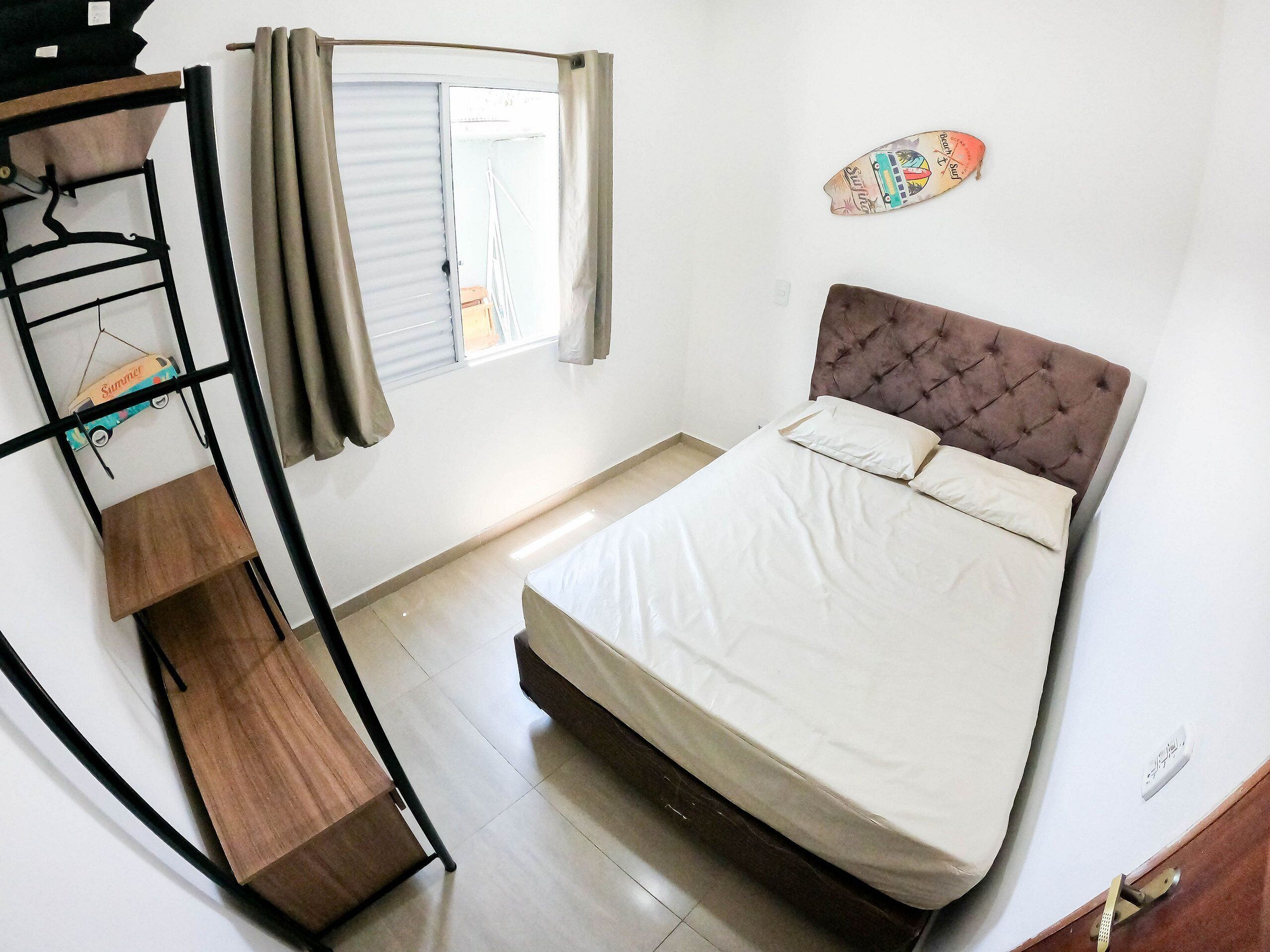 A bedroom with a bed, a wooden shelf, a window with curtains, and a wall decoration.