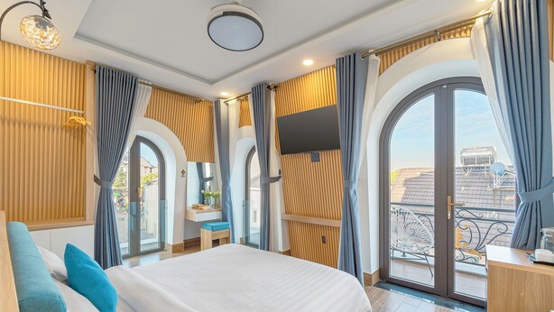 Una habitación de hotel moderna con una cama grande, un televisor montado en la pared y un balcón con vistas a la ciudad.